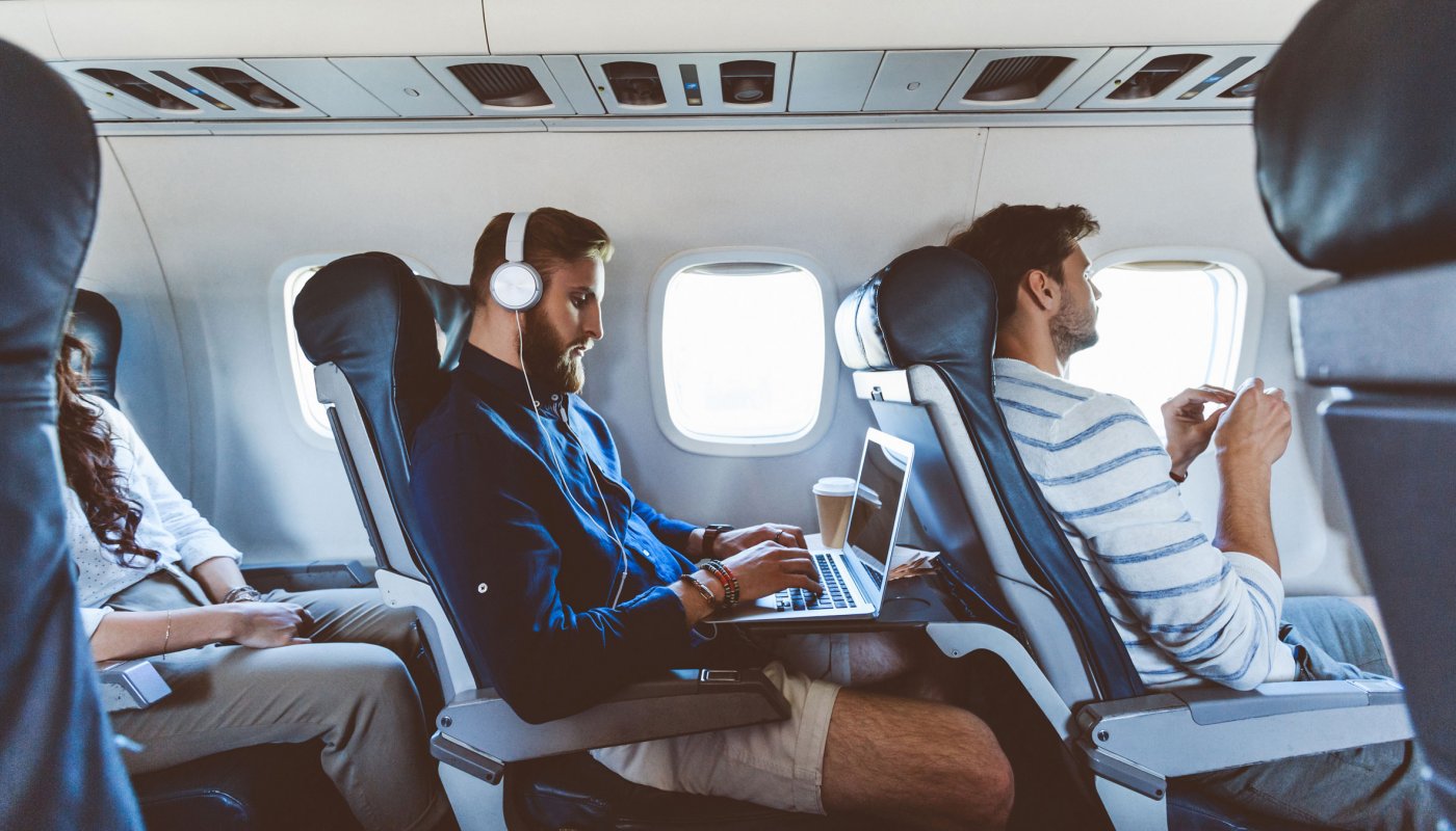 Un hipster portant un casque travaille sur son ordinateur dans un avion