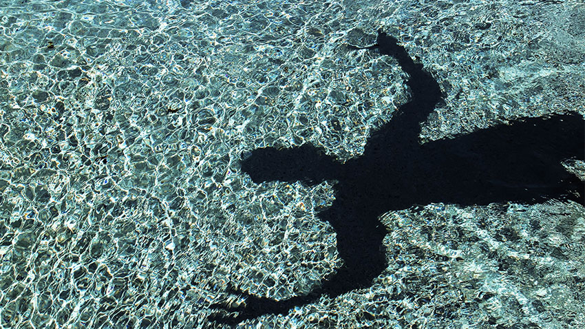 Reflet dans l'eau d'un homme qui gesticule autour d'une piscine