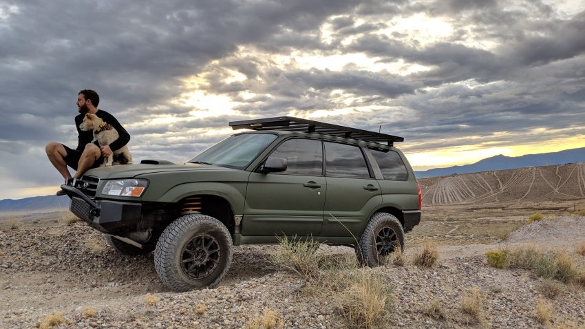 Un homme assis sur le capot de son 4x4 avec son chien dans un désert