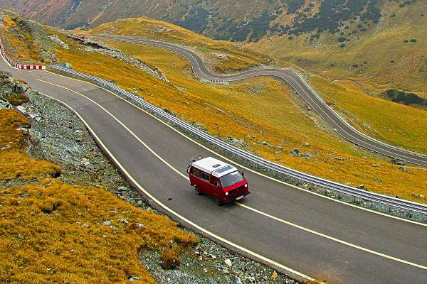 Un Van rouge roule sur une route de montagne