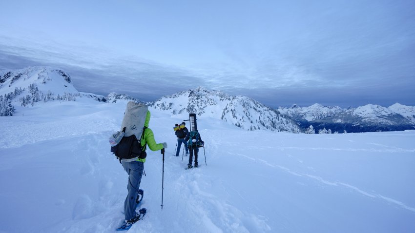 Trois randonneurs en raquette en montagne avec un piano dans le sac à dos