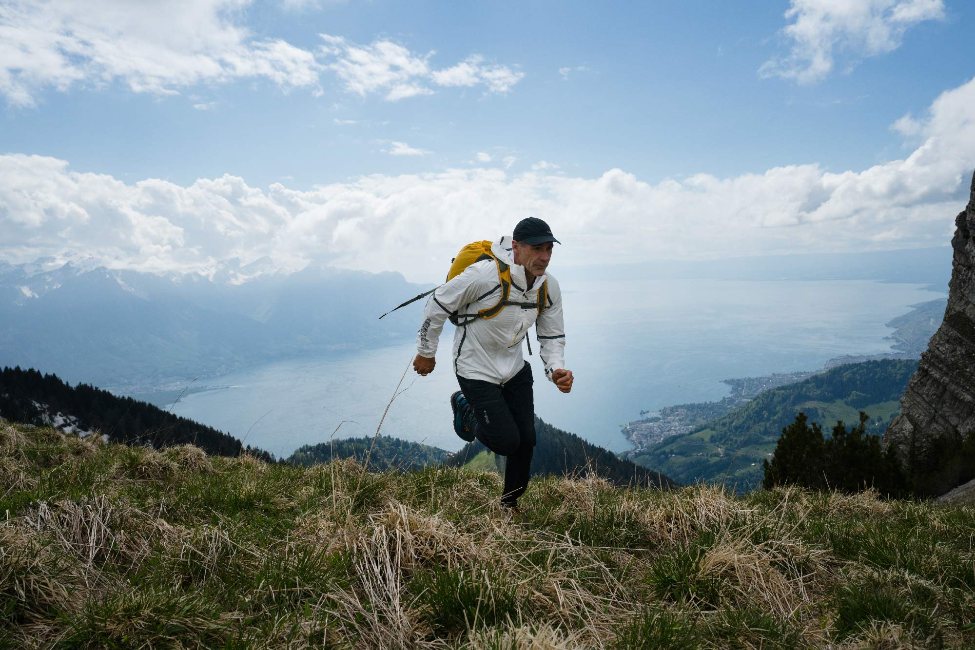 Mike Horn courant dans les montagnes Suisses avec vue lac en contrebas