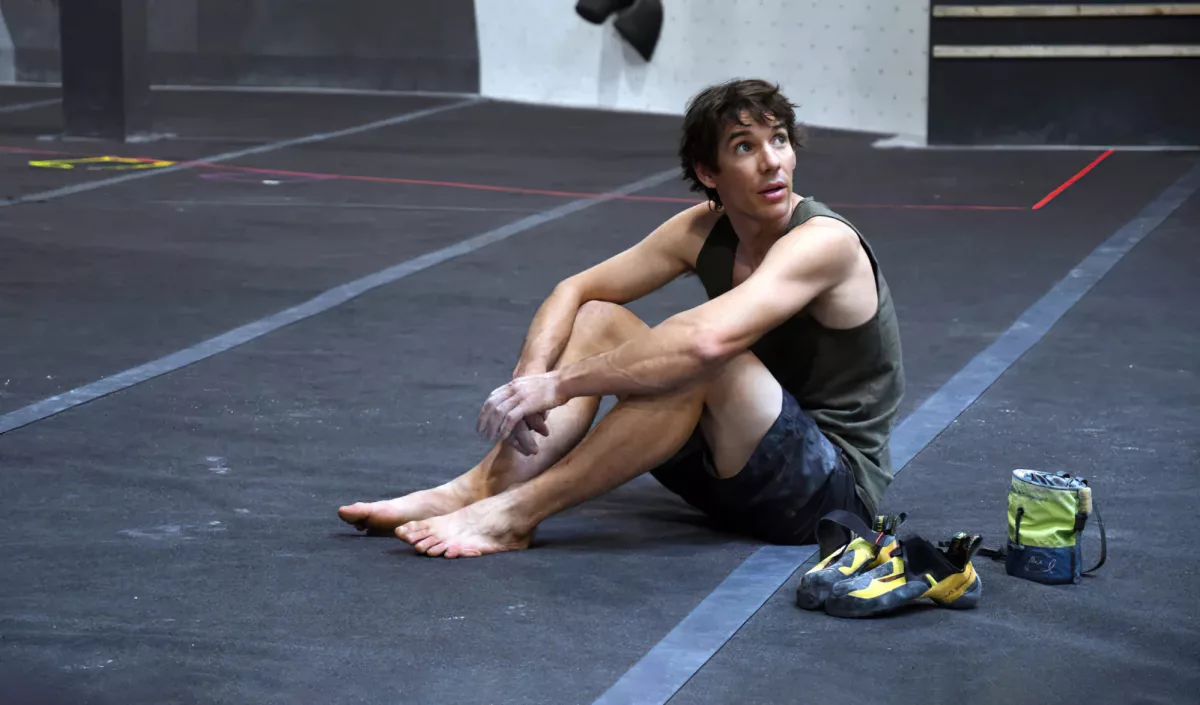 Alex Honnold assis au pied d'un mur d'escalade indoor