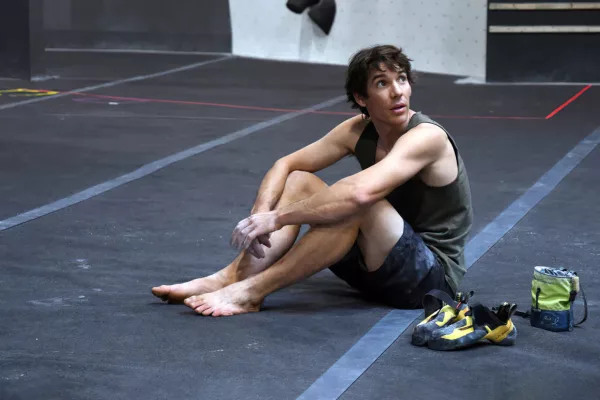 Alex Honnold assis au pied d'un mur d'escalade indoor