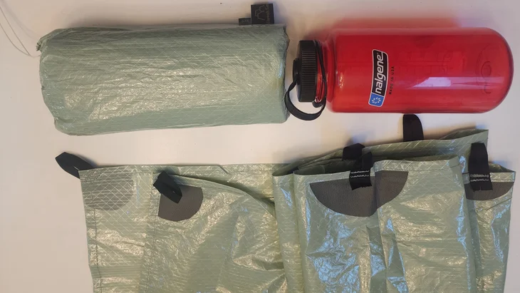 Le tarp 8×10 UltraTNT d'Elowah Outfitters enroulée à côté d'une bouteille Nalgene
